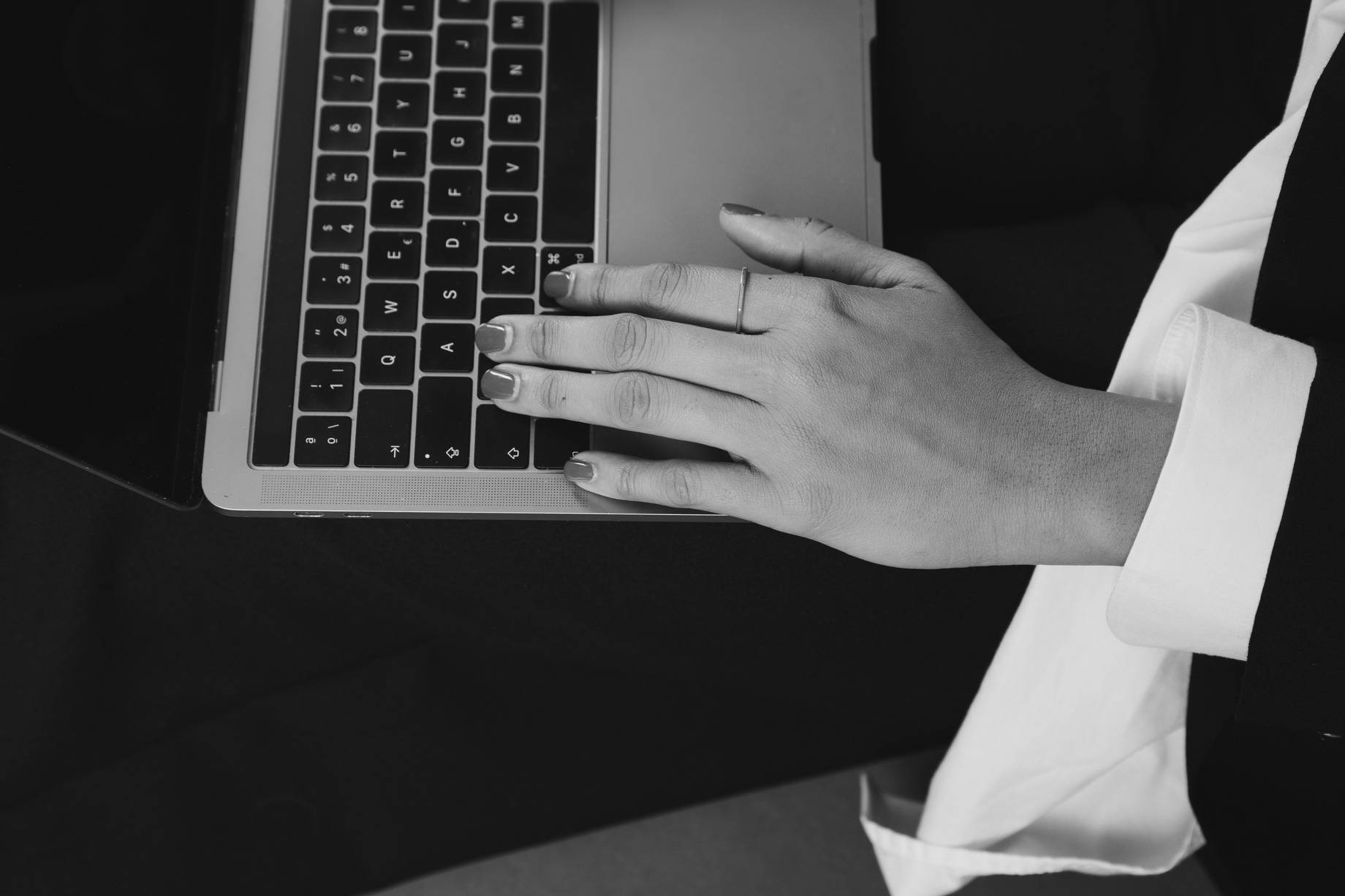 Mão com anel digitando em um notebook, em preto e branco.